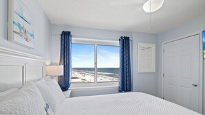 A bedroom with a large bed, a window with a view of the beach, and a door. - Tradewinds 701 by Liquid Life (Orange Beach)