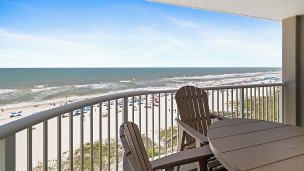 A balcony with a view of the beach, a table, and two chairs. - Tradewinds 701 by Liquid Life (Orange Beach)