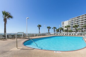 Uma piscina com cerca branca, palmeiras e um edifício alto ao fundo.