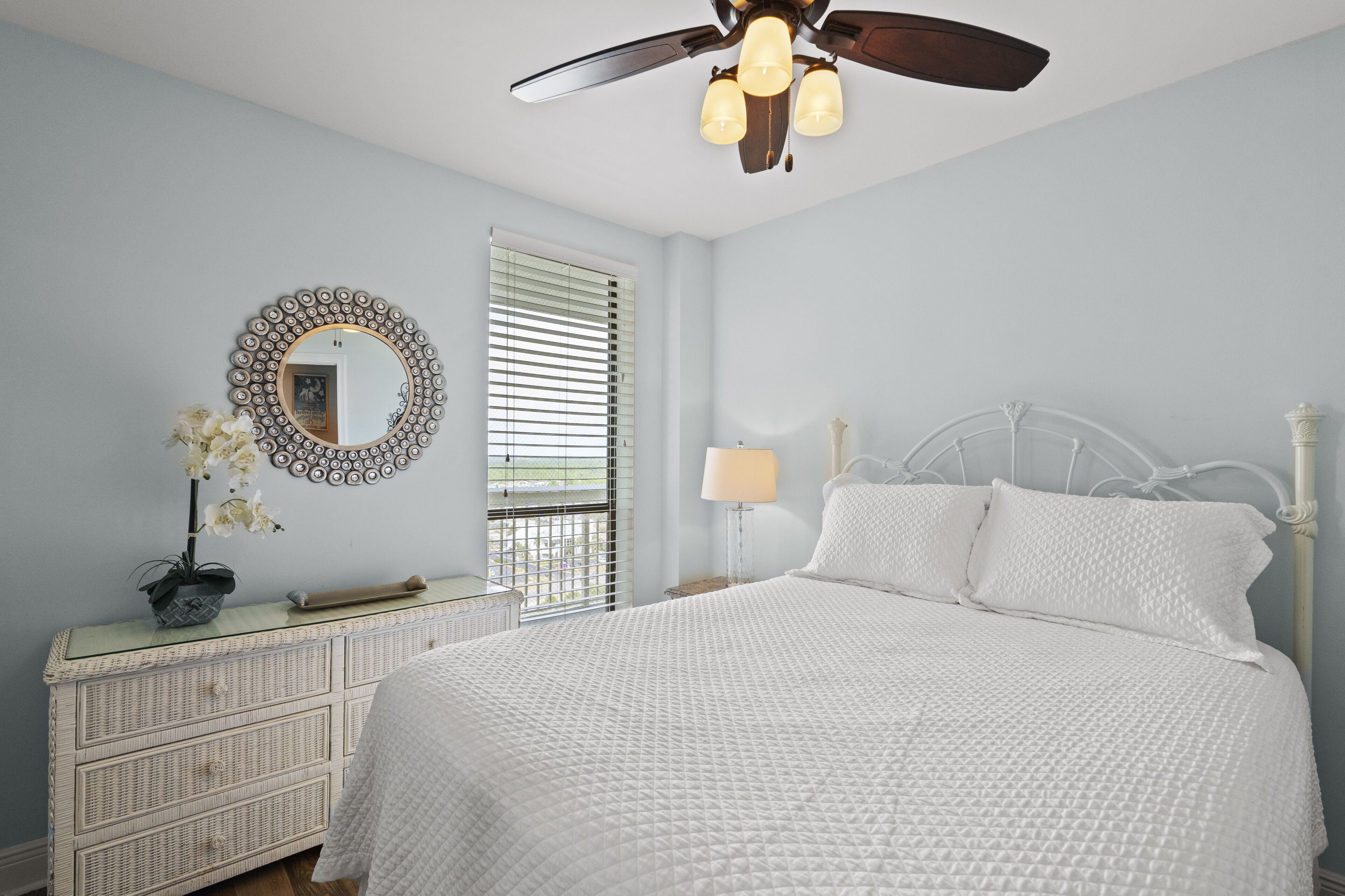 A bedroom with a bed, a dresser, a mirror, a ceiling fan, and a window with blinds.
