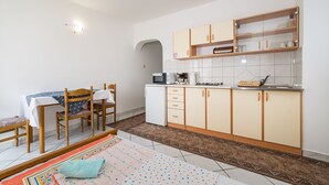 Une cuisine compacte équipée d’un four à micro-ondes, d’une machine à café et d’un petit réfrigérateur. On y trouve une table à manger avec des chaises et un tapis à motifs.