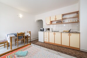 A compact kitchen with a microwave, coffee maker, and a small refrigerator. There is a dining table with chairs and a patterned rug.
