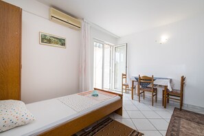 Una cama individual con cabecera de madera, una mesita con sillas, una ventana con persianas y un aire acondicionado instalado en la pared.