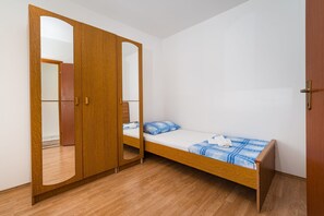 A bedroom with a wooden wardrobe, a single bed with a blue and white checkered bedspread, and a wooden floor.