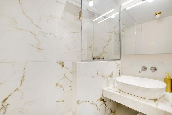 A bathroom with a marble vanity, a glass shower enclosure, and a white sink.
