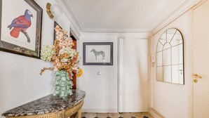 A hallway with a marble console table, a framed parrot illustration, a vase with flowers, a zebra framed picture, and a door with a glass panel.