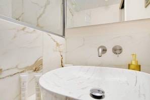 A bathroom with a marble sink, two faucets, and a gold soap dispenser.
