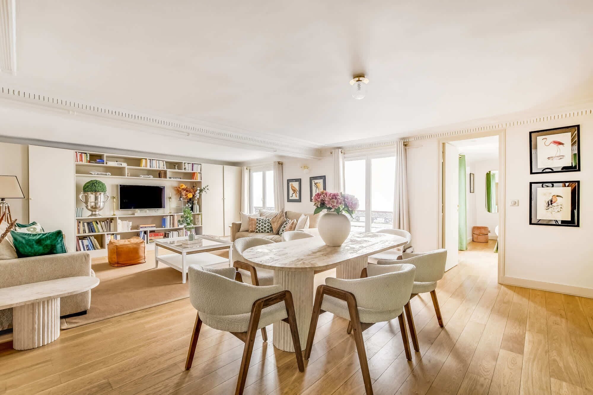 A spacious living room with a round dining table, comfortable seating, a bookshelf, and a television.