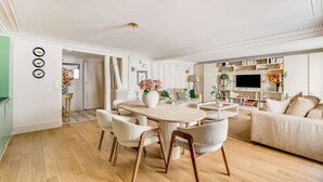 A spacious living room with a dining area, a sofa, a television, and a bookshelf.