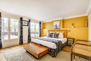 A hotel room with a bed, a bench, a chair, a window with curtains, and a wall with a picture. - A Breathtaking 2BR/2Ba in Opera (Paris)
