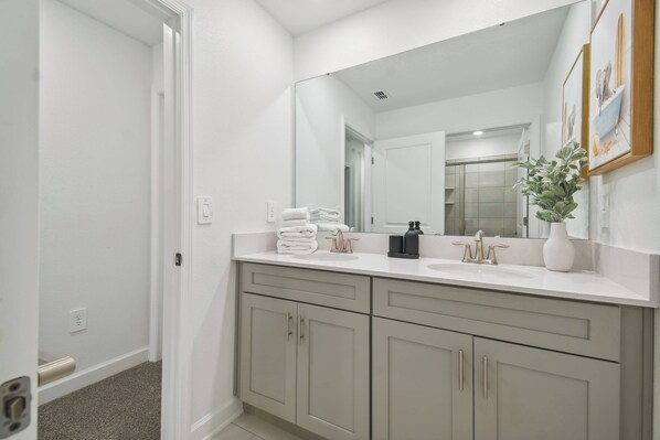 A modern bathroom with a white vanity, a large mirror, and a potted plant.