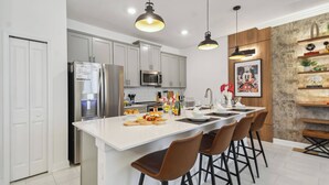 A modern kitchen with white cabinetry, stainless steel appliances, and a central island with bar stools. - Family 4BR Home w/ Pool at Storey Lake (Kissimmee)