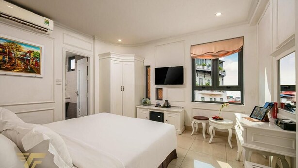 A hotel room with a large bed, a desk with a computer, a TV, and a window with a view of buildings. - Toan Thang Hotel by Bay Luxury (Hanoi)