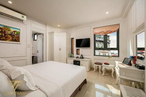A hotel room with a large bed, a desk with a computer, a TV, and a window with a view of buildings. - Toan Thang Hotel by Bay Luxury (Hanoi)