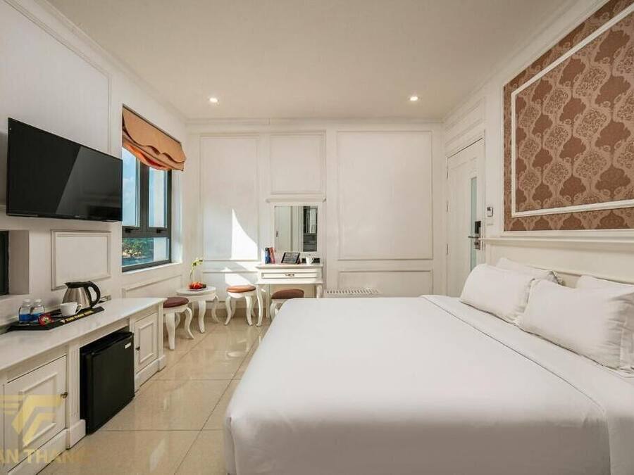 A hotel room with a large bed, a television, a desk with a chair, and a small table with a chair.