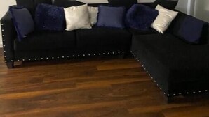 Ein schwarzes Ecksofa mit Zierknöpfen auf Holzdielen.