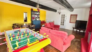 A living room with a foosball table, a red sofa, and a television. - Cosy rural 5 bedroom home with games room, pet friendly, garden, bbq! (Ger)