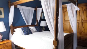 A four-poster canopy bed with white bedding and blue patterned pillows, a wooden nightstand with a lamp, and a wooden wardrobe in a room with blue walls. - Cosy rural 5 bedroom home with games room, pet friendly, garden, bbq! (Ger)