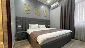 A modern bedroom with a large bed, a nightstand, and a dresser. There are three wall-mounted light fixtures and an air conditioning unit. - Days Inn Hotel (Yerevan)