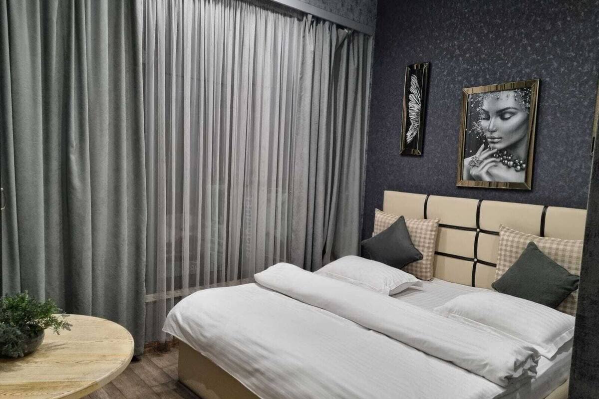 A bedroom with a bed, curtains, a round table, and two wall art pieces.