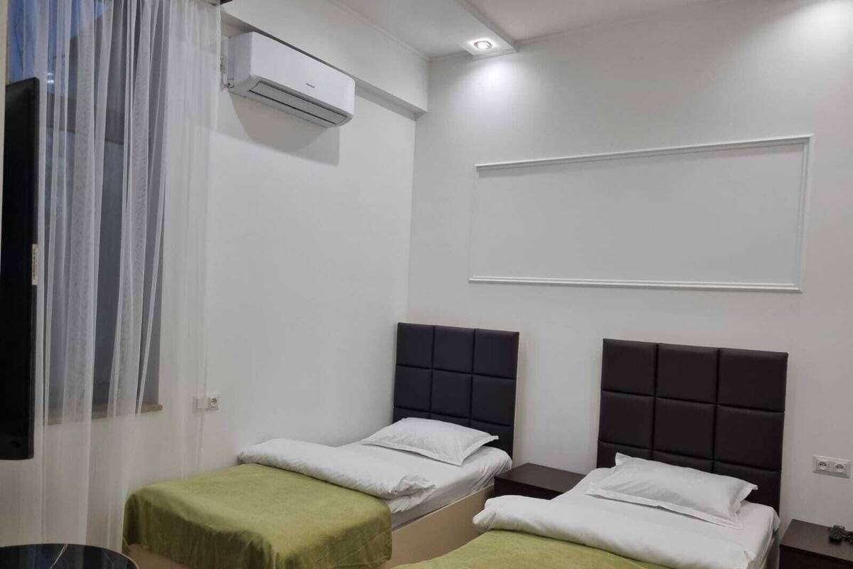 A hotel room with two single beds, a small table, and an air conditioning unit on the wall.