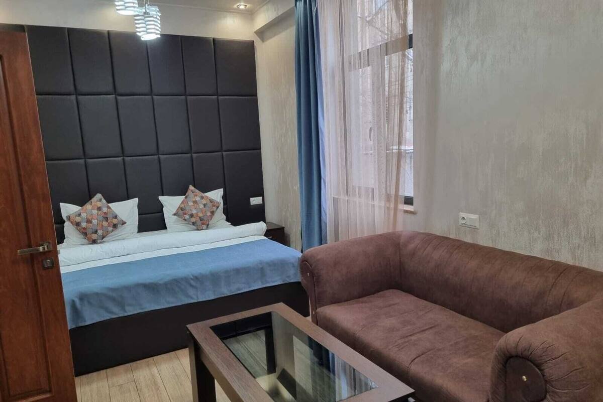 A bedroom with a bed, a brown sofa, and a glass-top coffee table.