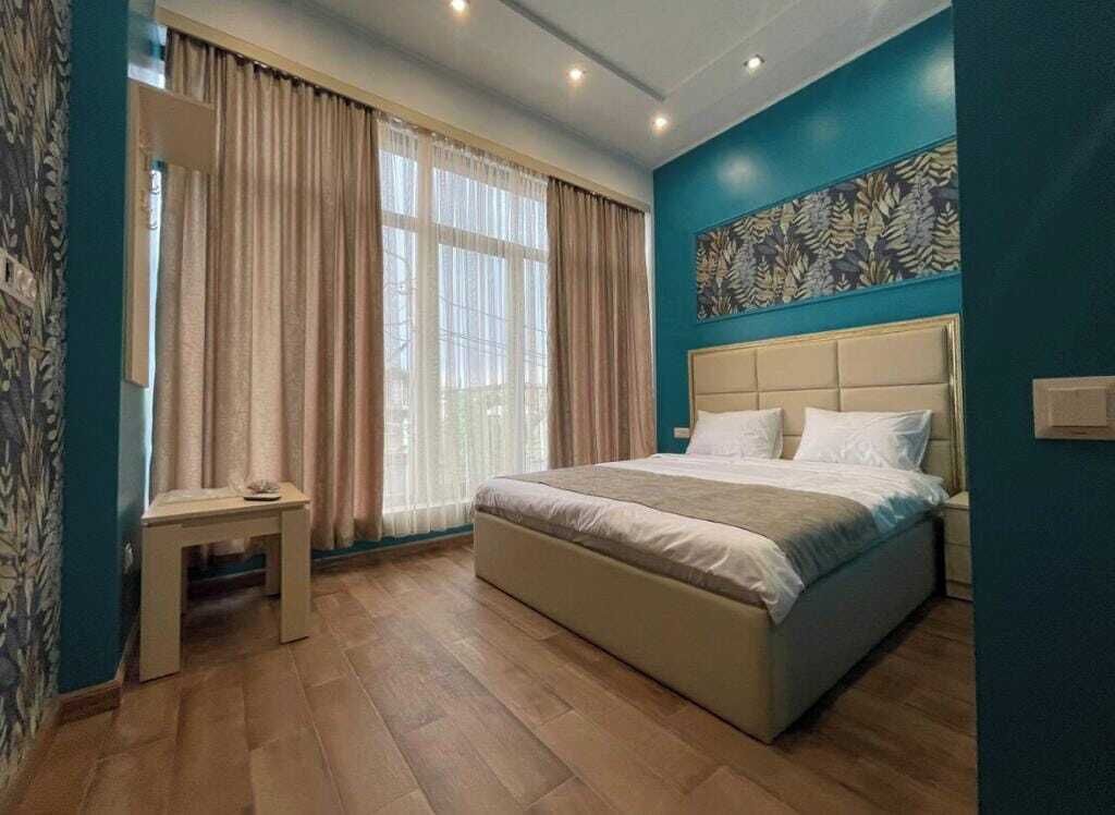 Un dormitorio con una cama grande, una mesita de noche, una ventana con cortinas y una pared con estampado floral.