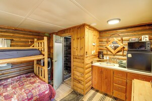 Una habitación tipo cabaña compacta con literas, una kitchenette con refrigerador, microondas y pileta, y un baño pequeño con ducha.
