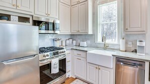 A modern kitchen with white cabinetry, stainless steel appliances, and a window with a view of the city. - Historic Charnwood Guest House- 1 Mile to Downtown (Tyler)