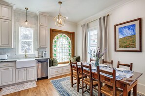 A kitchen with white cabinets, a built-in dishwasher, and a dining area with a wooden table and chairs. - Historic Charnwood Guest House- 1 Mile to Downtown (Tyler)