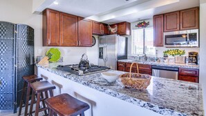 A kitchen with wooden cabinets, a stainless steel refrigerator, a microwave, and a granite countertop. - Palm Desert Condo w/ Patio & Golf Course Views! (Palm Desert)
