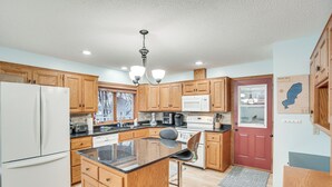 A kitchen with wooden cabinets, a white refrigerator, a microwave, and a bar stool.