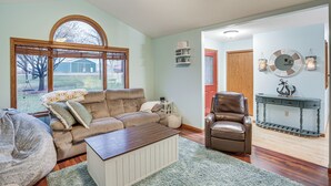 A living room with a brown leather sofa, a white armchair, and a wooden coffee table. There is a large window with a view of the outdoors.