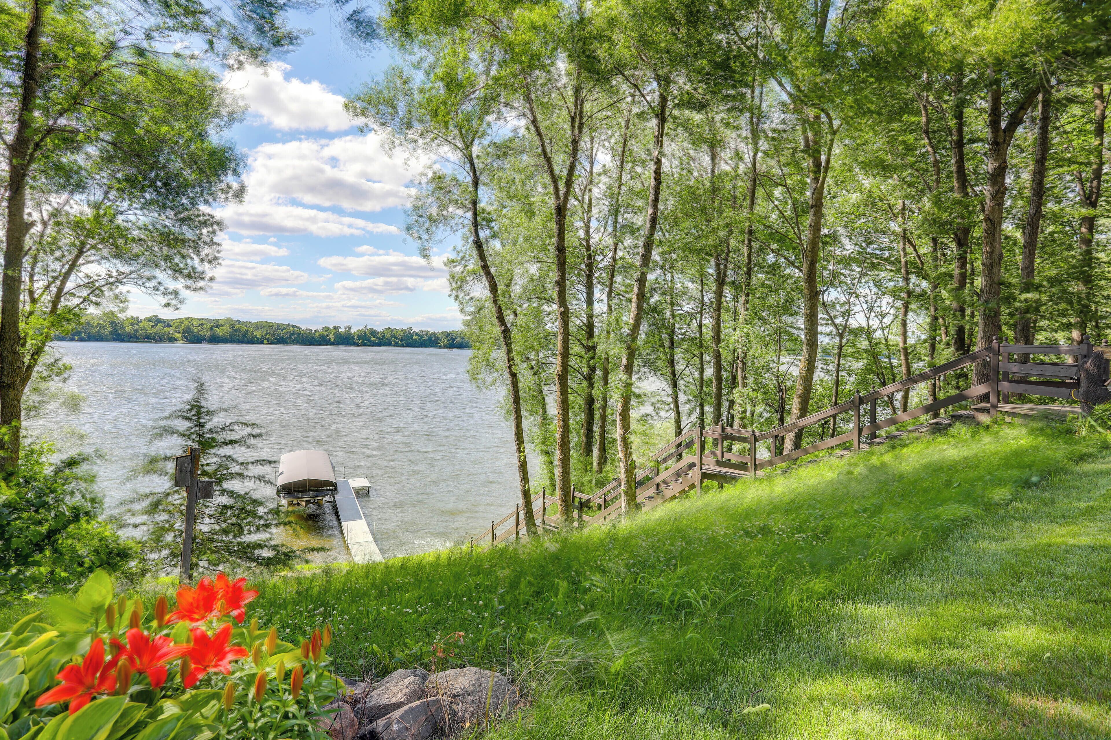 A lakeside view with a dock, wooden stairs, and lush greenery.