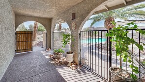 A covered patio area with a pool, potted plants, and a gate.
