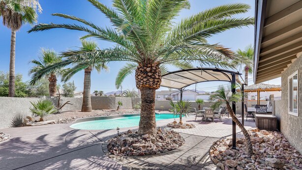A pool area with palm trees, a covered patio, and a stone pathway.