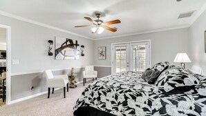 A bedroom with a bed, ceiling fan, artwork, and a window.