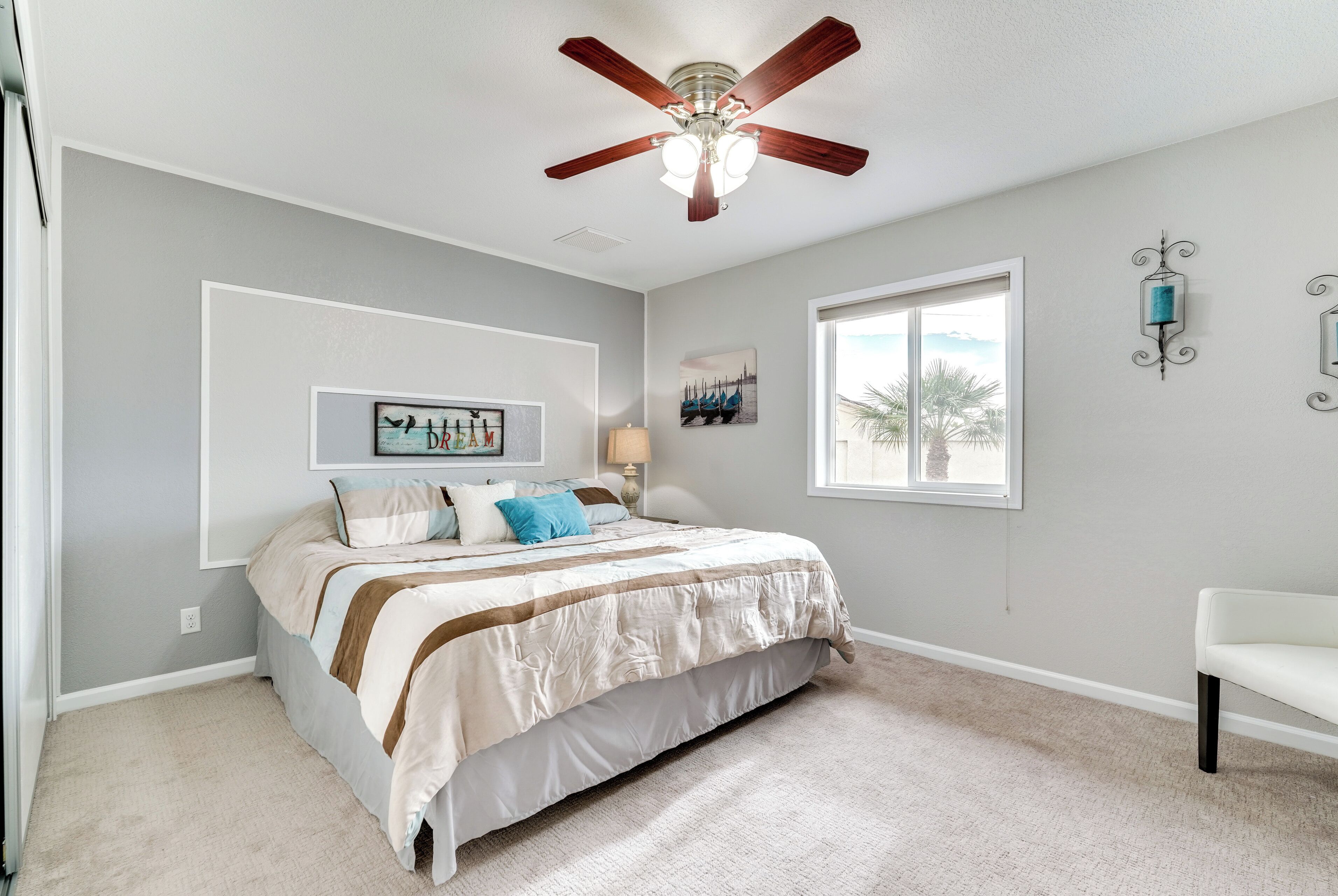 Un dormitorio con una cama, ventilador de techo, ventana y lámpara de pared.