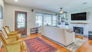 Ein Wohnzimmer mit einer Couch, Sesseln, einem Kamin und einem an einer Steinwand befestigten Fernseher.