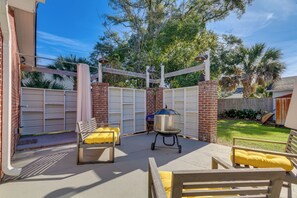A patio with two wooden chairs and a grill, surrounded by a brick wall and a wooden fence. - Pensacola Home in Historic East Hill Neighborhood (Pensacola)