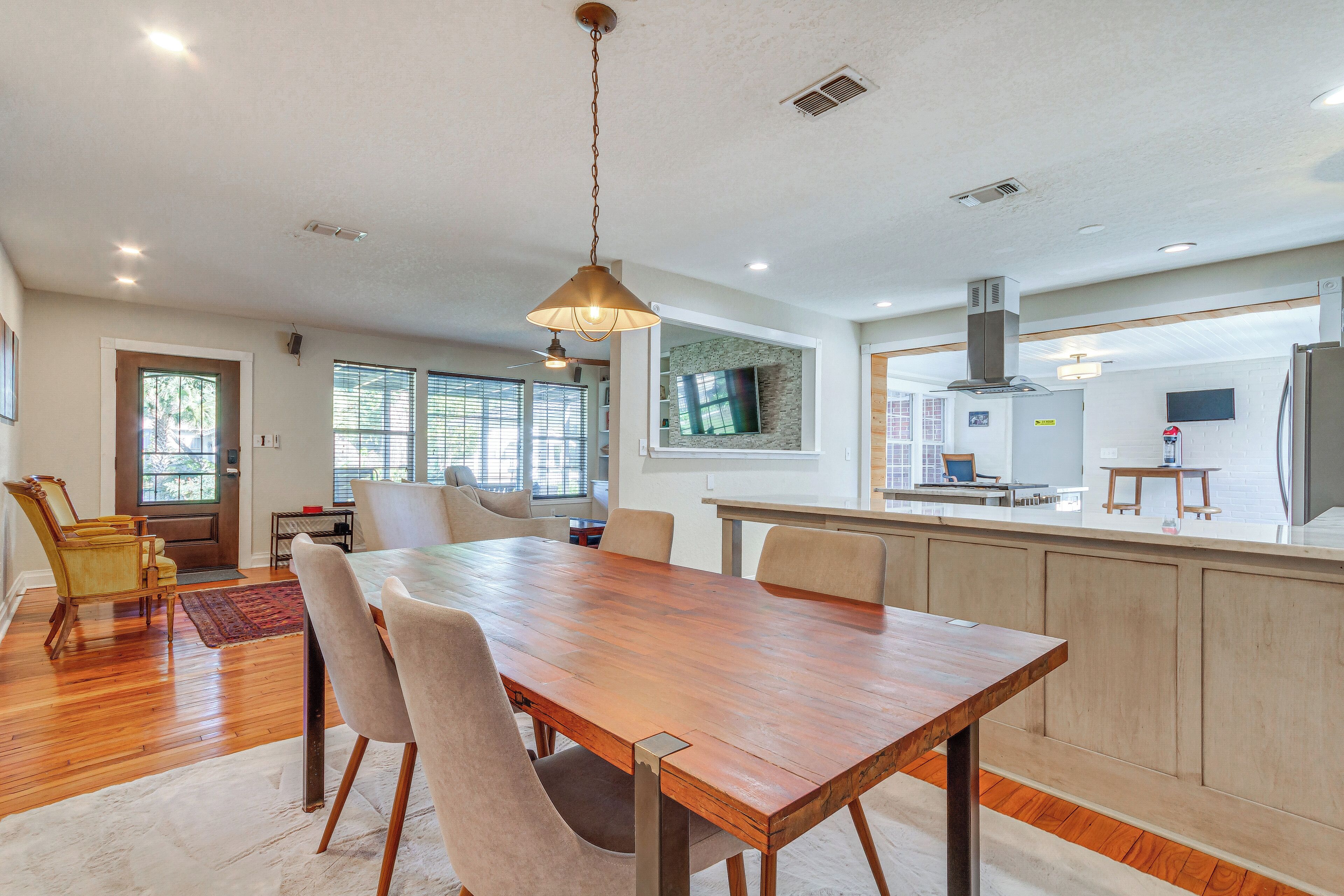 A spacious dining area with a wooden table and chairs, a hanging light fixture, and a view into the kitchen area.