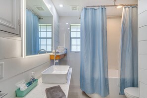 A modern bathroom with a white sink, a bathtub, and a shower curtain. - Pensacola Home in Historic East Hill Neighborhood (Pensacola)