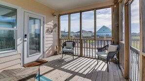 A covered porch with two wicker chairs, a door with a glass panel, and a view of houses in the background. - Crystal Beach Home w/ Covered Patio: Pets Welcome! (Port Bolivar)