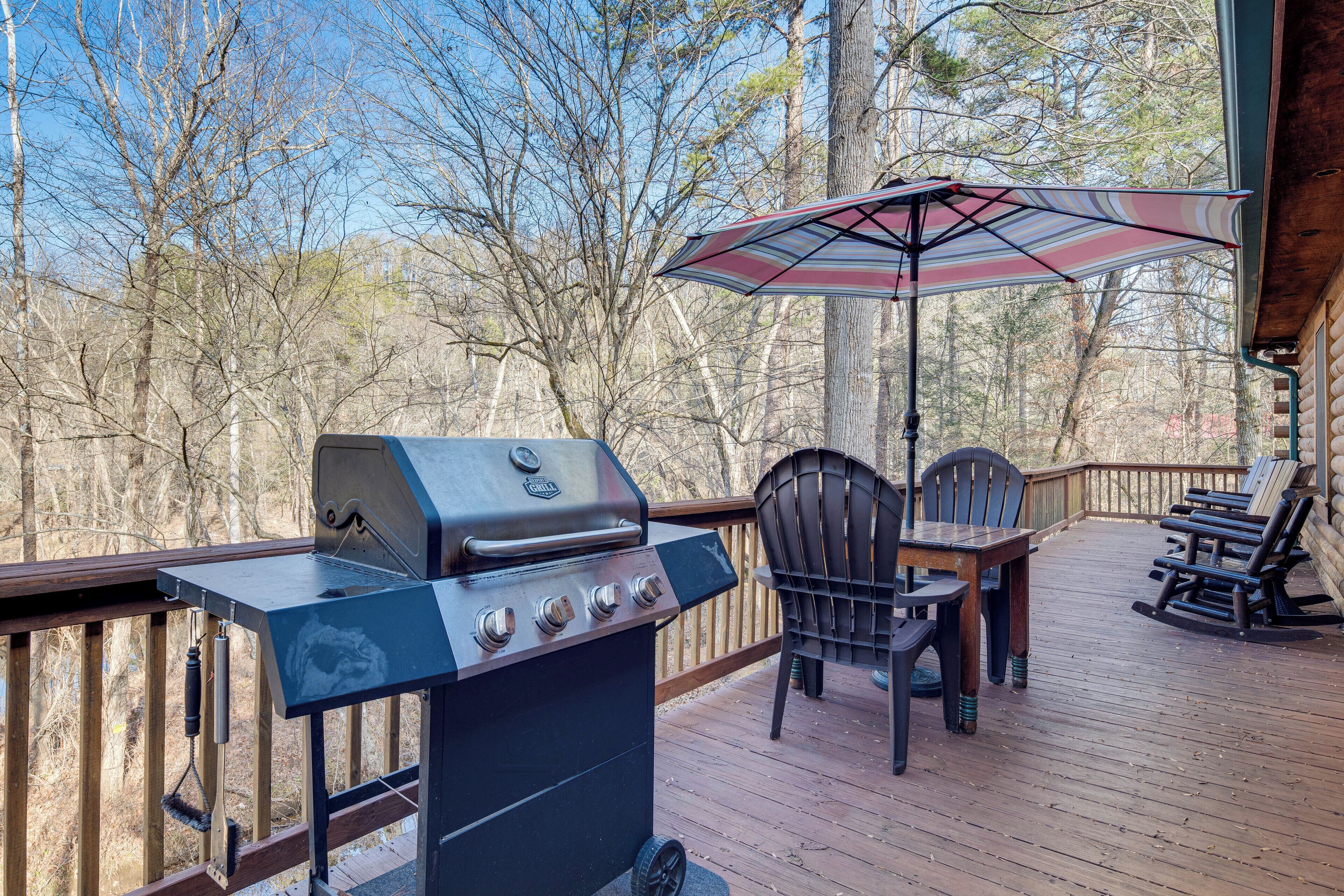 A wooden deck with a grill, chairs, and an umbrella.