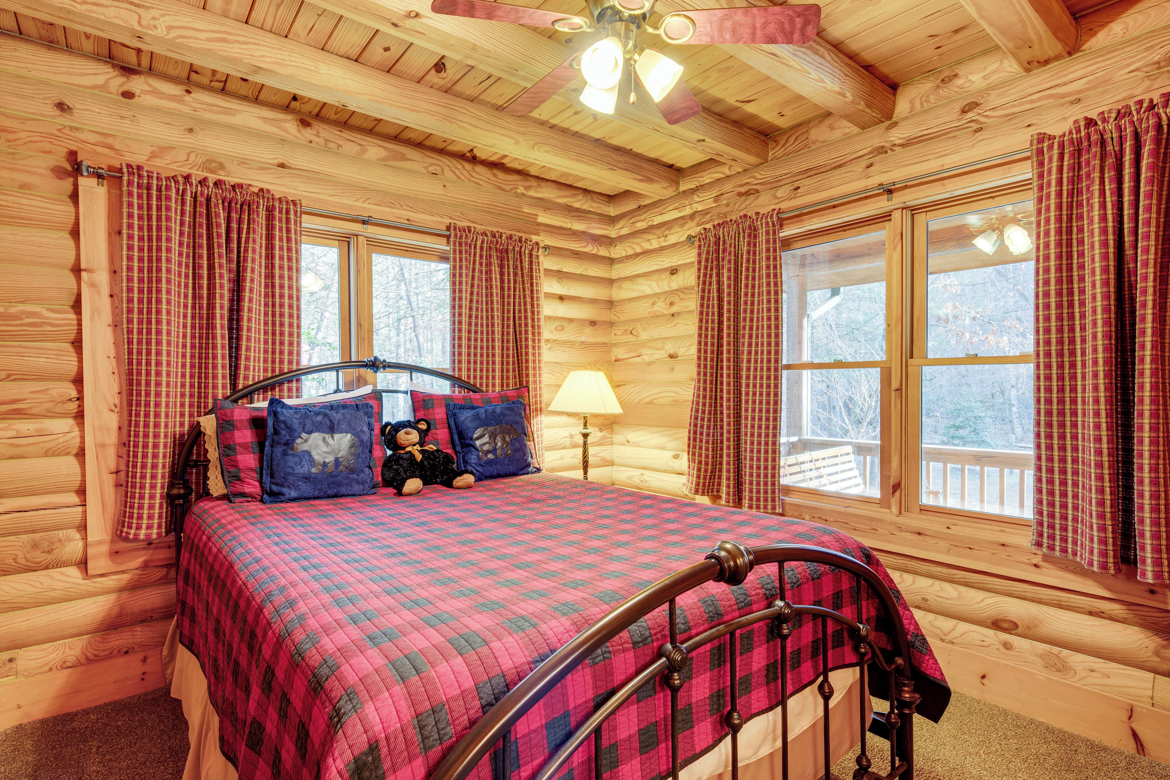 Ein gemütliches Schlafzimmer in einer Blockhütte mit Bett, Kissen, einer Lampe und Karosvorhängen.