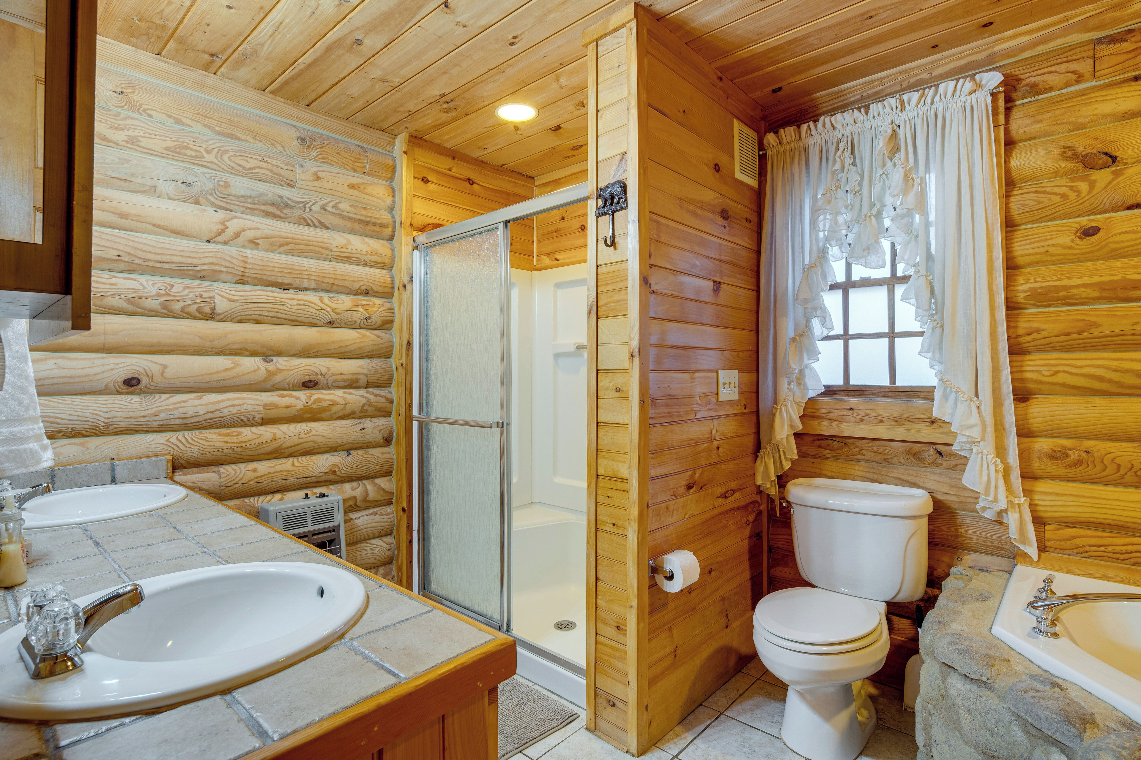 Ein Badezimmer einer Holzhütte mit Dusche, Toilette und Waschbecken, inklusive einem Becken aus Stein.