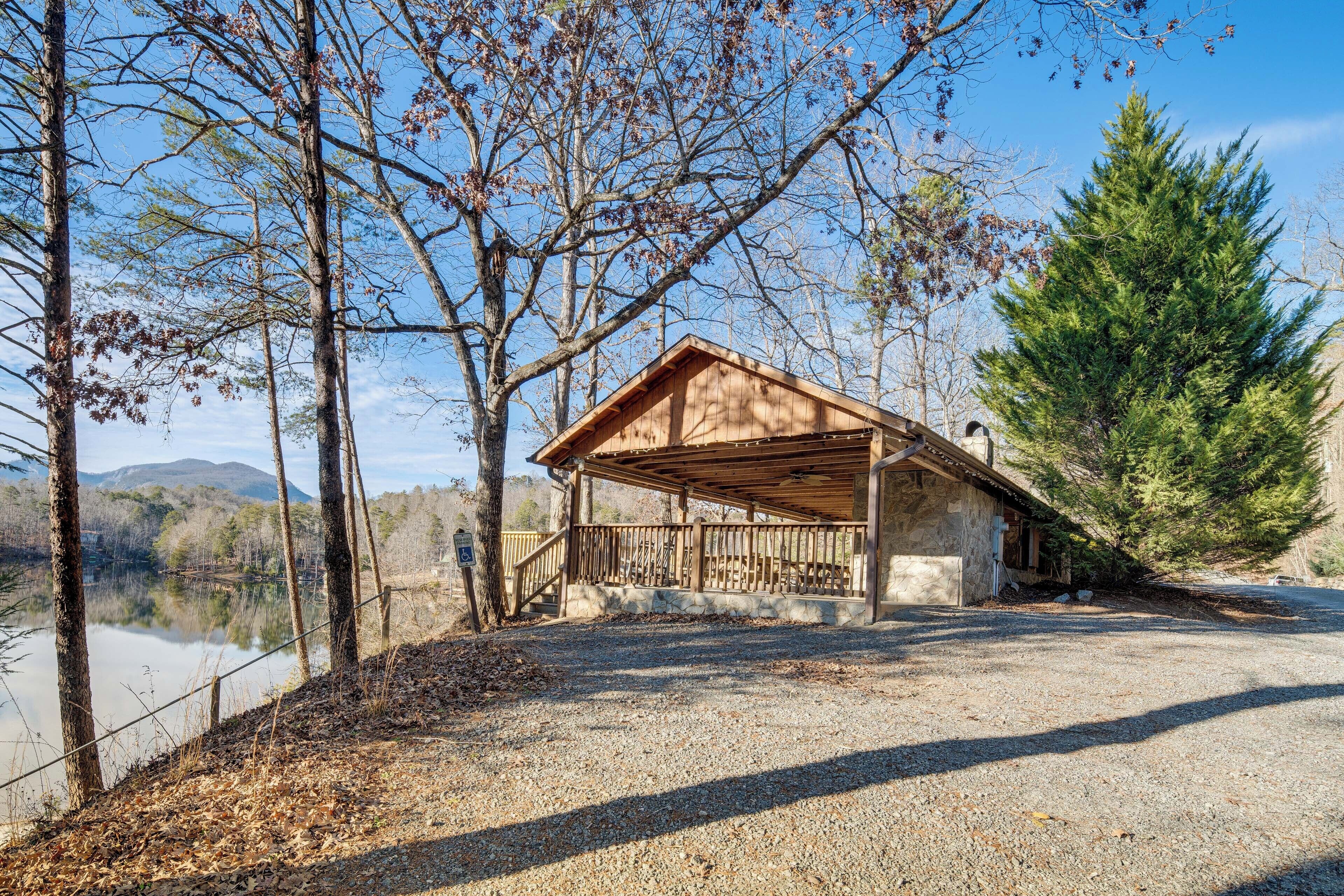 A rustic cabin with a wooden deck, surrounded by trees and a lake.
