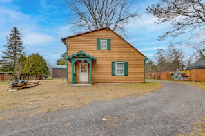 A wooden house with a front porch, a garage, and a gravel driveway.