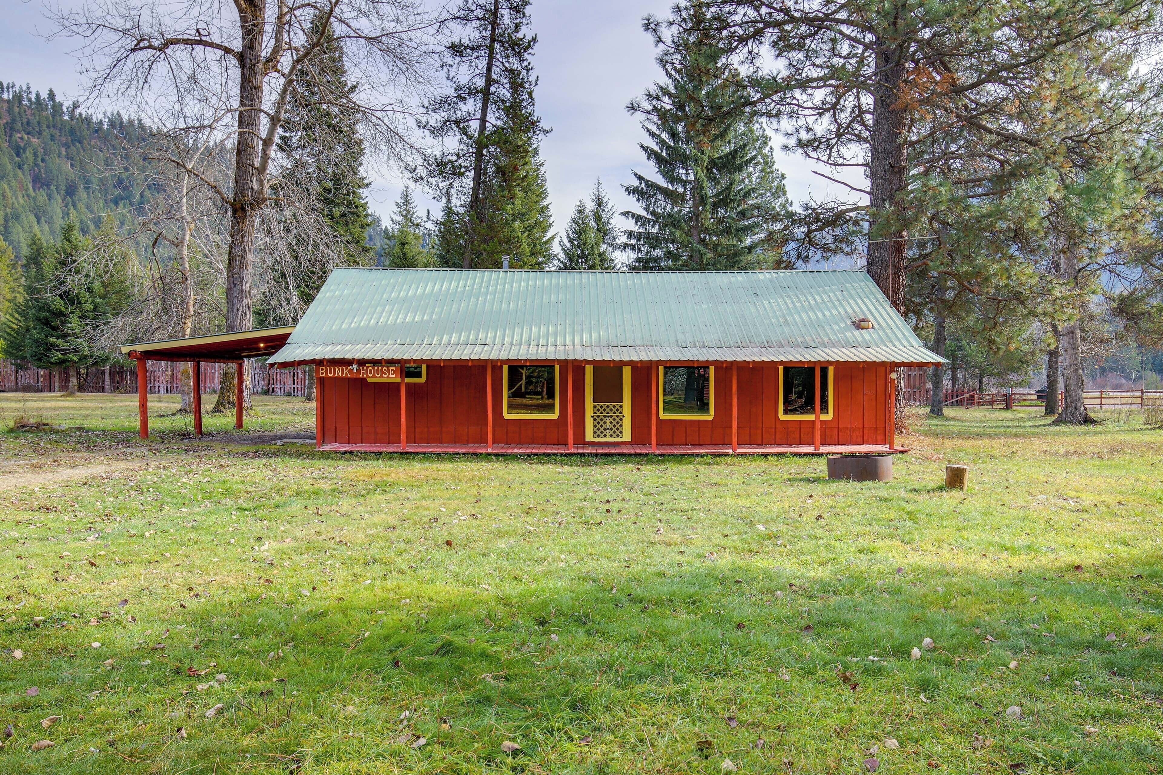 A rustic cabin with a green roof, surrounded by tall trees and a grassy field.