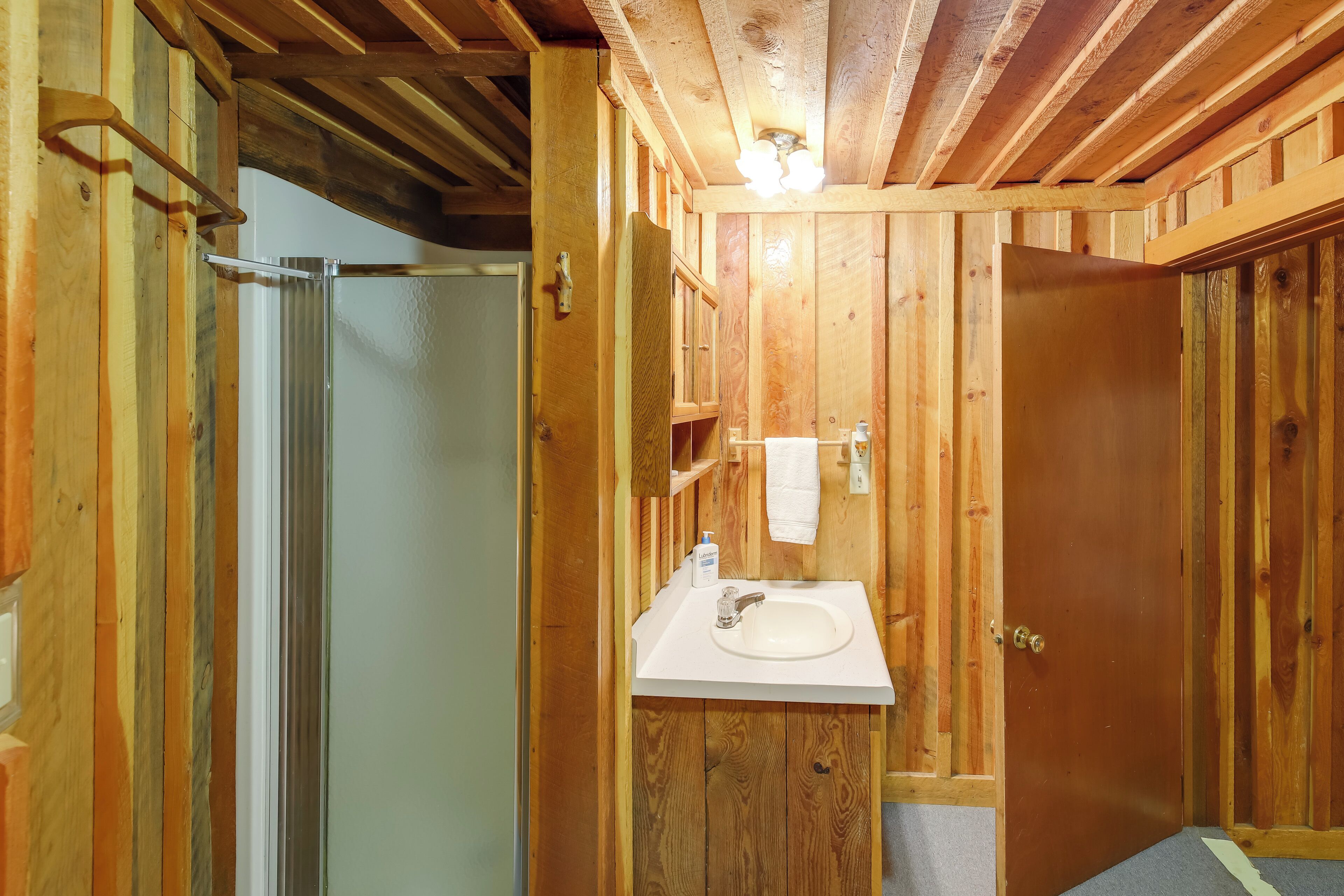 Un baño de madera con ducha, lavabo y una toalla colgada en la pared.